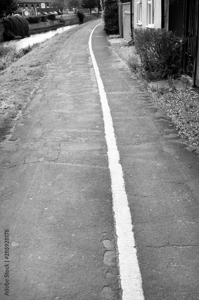 Black and white photo. The pedestrian sidewalk is divided into two parts with a white stripe Black and white photo. The pedestrian sidewalk is divided into two parts with a white stripe