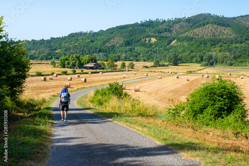 Un viaggiatore solitario con lo zaino in spalla cammina lungo una classica strada di campagna italiana