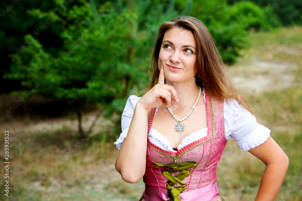 Naklejka premium young woman in dirndl standing outdoors and looking thoughtfull