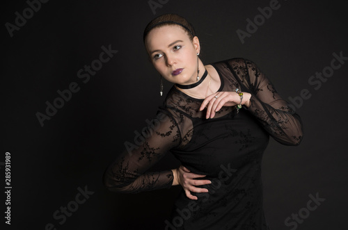 Beautiful young woman in black dress posing in studio with black background