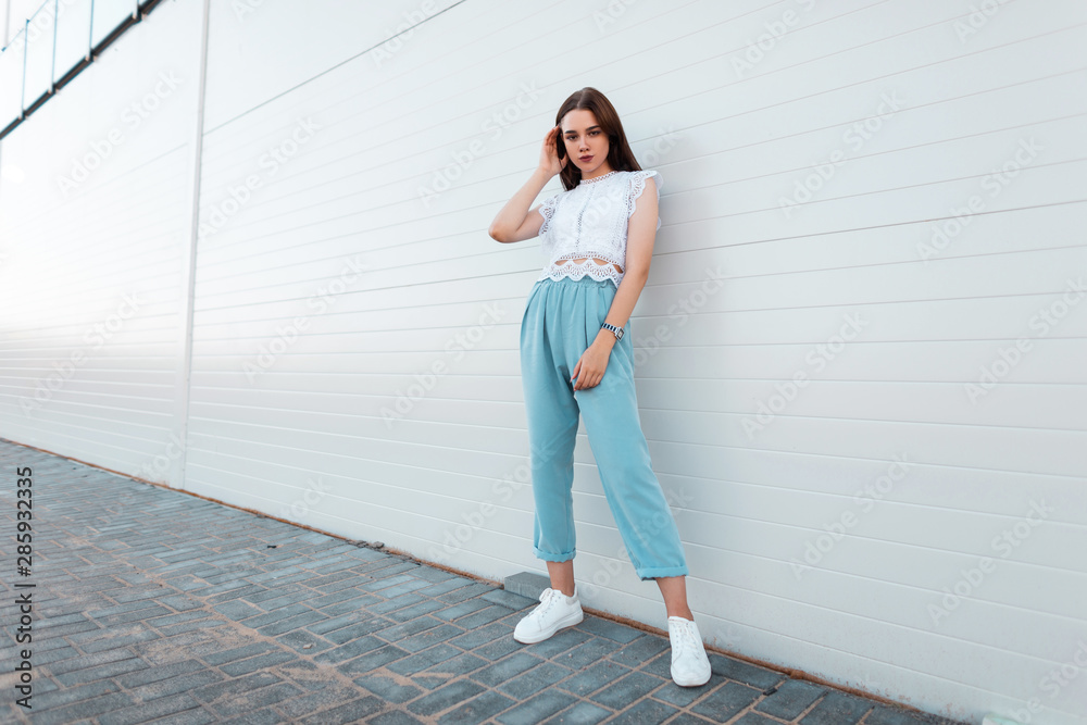 Beautiful young woman model in a stylish lace top in blue pants in white  sneakers is