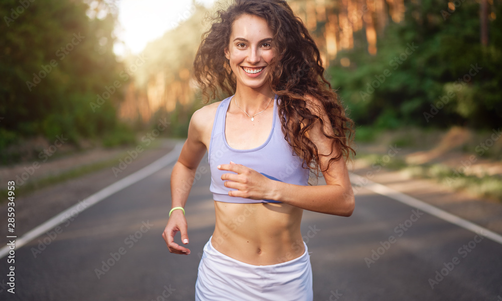 Beautiful caucasian young girl athlete runs sunny summer day on asphalt road in the forest. Beautiful caucasian young girl athlete runs sunny summer day on asphalt road in the forest.