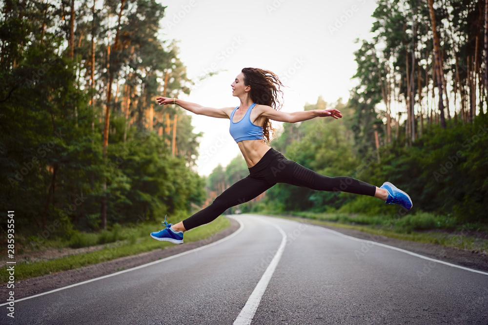 young beautiful brunette girl jumping in twine with background asphalt road and pine forest young beautiful brunette girl jumping in twine with background asphalt road and pine forest