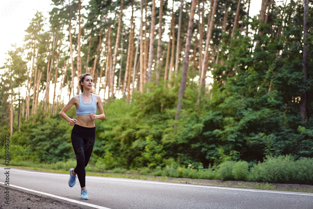 Beautiful caucasian young girl athlete runs sunny summer day on asphalt road in the forest. Beautiful caucasian young girl athlete runs sunny summer day on asphalt road in the forest.