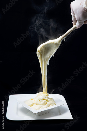 A low contrast artistic hero shot of fresh hot cheese being served on to a platter with smoke coming off the stretched cheese on a minimal white background from a flat horizontal perspective