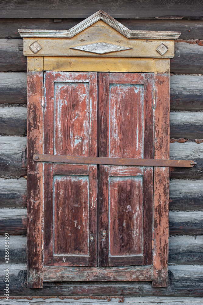 Old casement closed carved window of a house in Russian Siberia. Log house. Yellow with red color of the window. Vertical frame. Old casement closed carved window of a house in Russian Siberia. Log house. Yellow with red color of the window. Vertical frame.