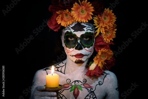 Fototapeta Naklejka Na Ścianę i Meble -  Woman bodypaint in day of the death ghoast decorate with flowers holding candle light in dark background