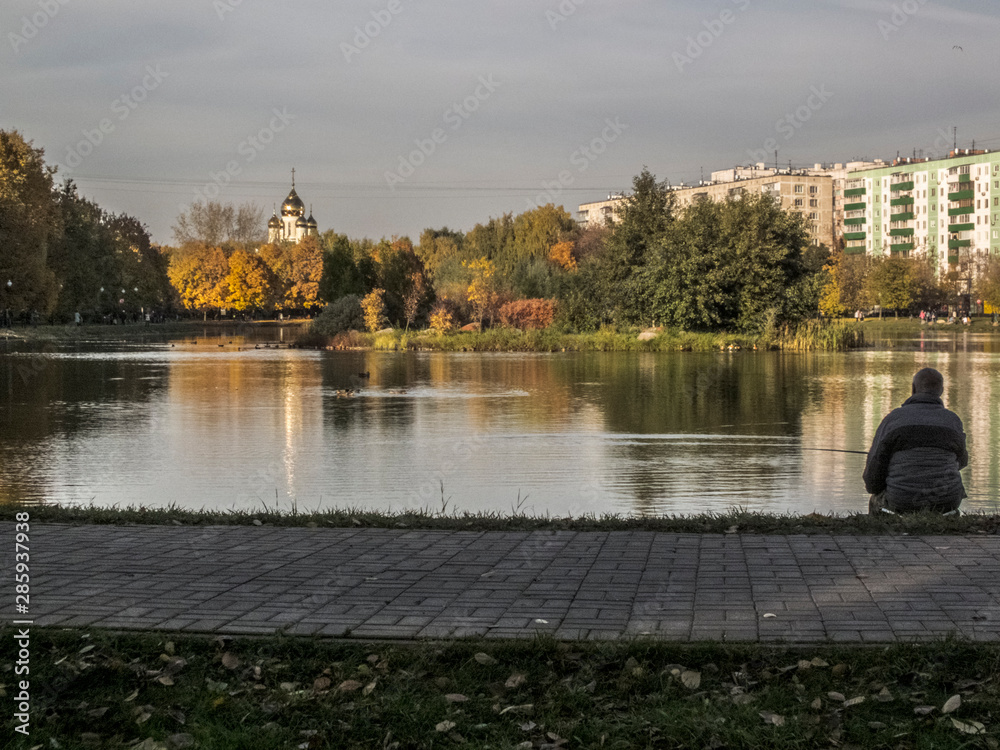 Man fishing. Autumn time, autumn in the city, urban autumn landscape with a pond, people walking and other fun
