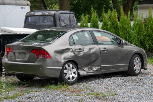 Gray car in a junk yard with damage to the rear panel, door and tire of a gray car due to an automobile accident