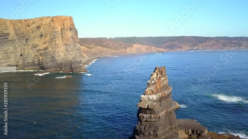Aerial, orbit, drone shot, around a huge rock, on the Atlantic ocean, near Pedra da Agulha, Arrifana Beach, in the background, on a sunny day, in Vicentina coast national park, in Portugal