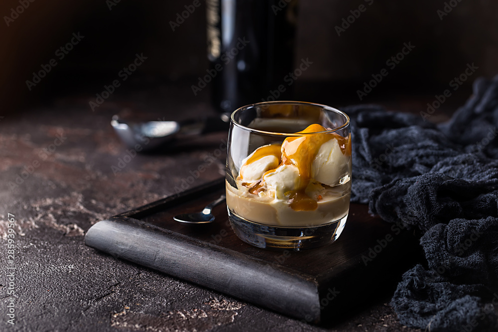 Ice cream with caramel topping and Irish cream liqueur in a glass over dark background. - obrazy, fototapety, plakaty 