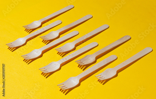 Many eco-friendly wooden forks on yellow background. Minimalistic eco concept. Pop art