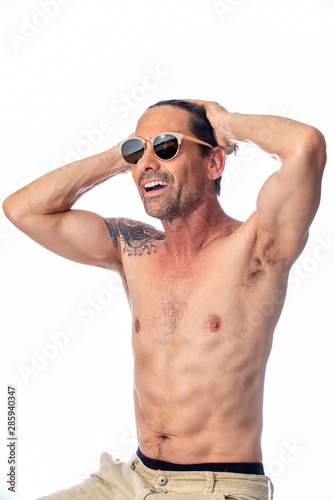 Healthy, shirless, muscular, middle aged man smiling while feeling handsome wearing reflective aviator sunglasses in high key background.