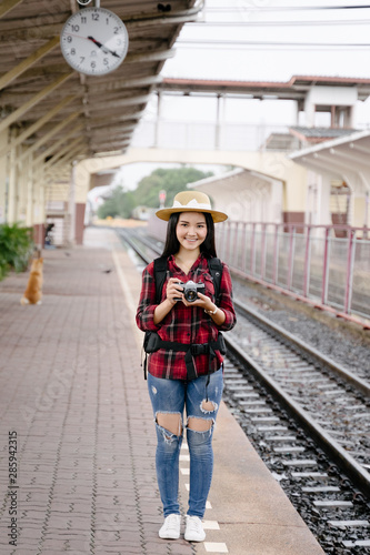 Young beautiful female travel photographer enjoys taking photo during her trip at railway station. Asian woman travel with camera having fun making pictures while waiting for train.