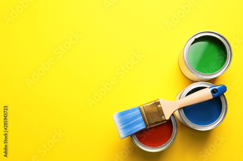 Open paint cans, brush and space for text on color background, top view