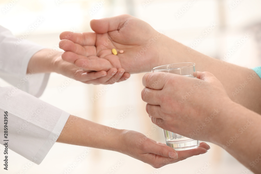 Nurse giving glass of water and pills to elderly man against blurred background, closeup. Assisting senior generation Nurse giving glass of water and pills to elderly man against blurred background, closeup. Assisting senior generation