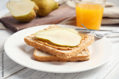 Slice of bread with peanut butter and pear on white wooden table