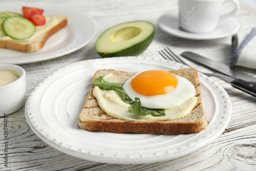 Slice of bread with fried egg, spread and arugula on white wooden table