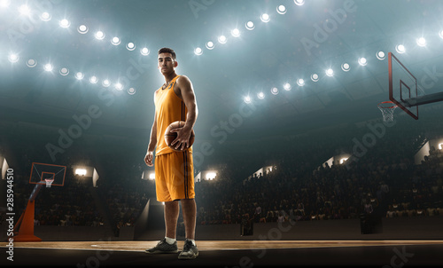 Basketball player in sports uniform on empty floodlit basketball court with the ball