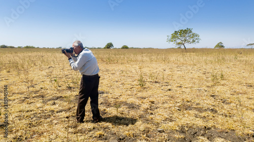 Old male photographer taking a photo savanna view