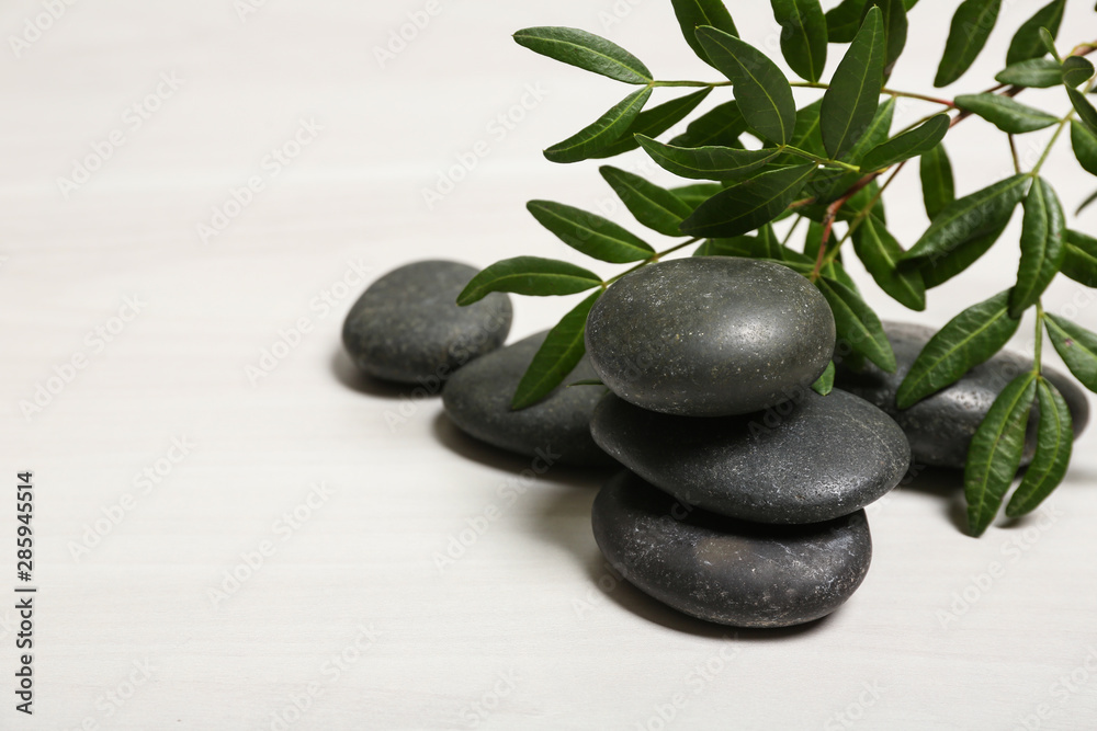 Naklejka premium Spa stones and green leaves on white table, space for text