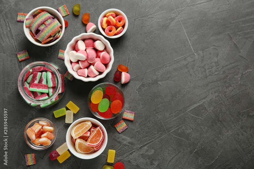 Flat lay composition with bowls of different jelly candies on black stone background. Space for text Flat lay composition with bowls of different jelly candies on black stone background. Space for text