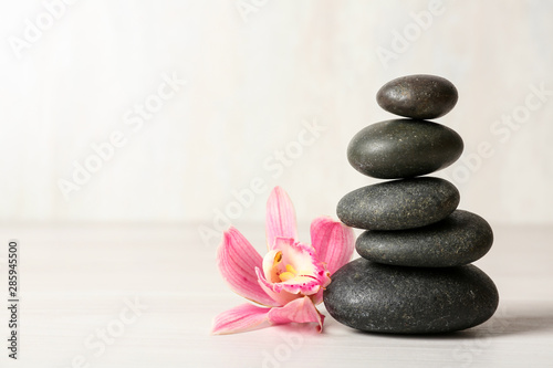 Stack of spa stones and flower on table against white background, space for text