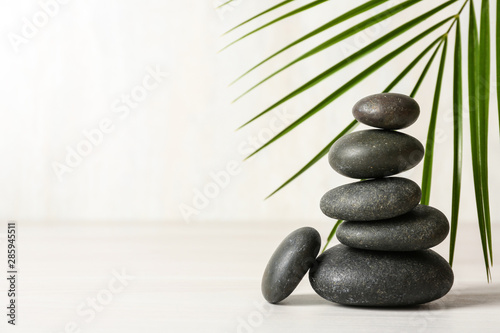 Stack of spa stones and palm leaf on table against white background, space for text