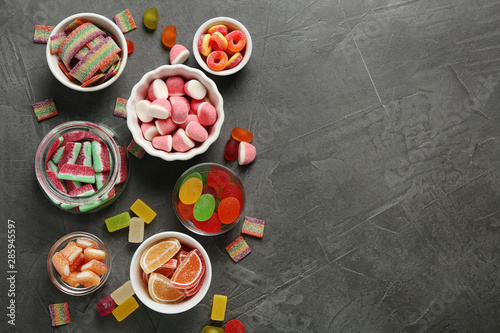 Flat lay composition with bowls of different jelly candies on black stone background. Space for text