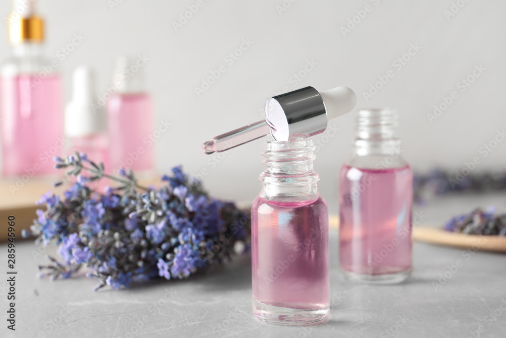 Bottles of essential oil and lavender flowers on stone table
