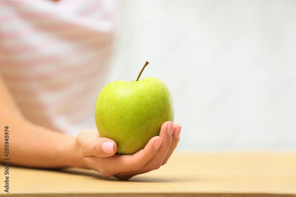 Woman holding fresh green apple at table, closeup. Space for text