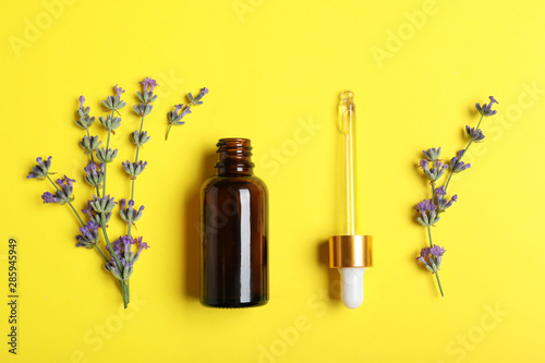 Bottle of essential oil and lavender flowers on yellow background, flat lay