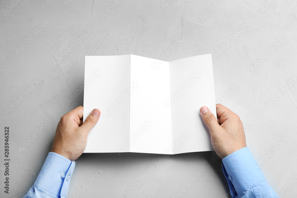 Young man holding blank brochure at grey table, top view. Mock up for design Young man holding blank brochure at grey table, top view. Mock up for design