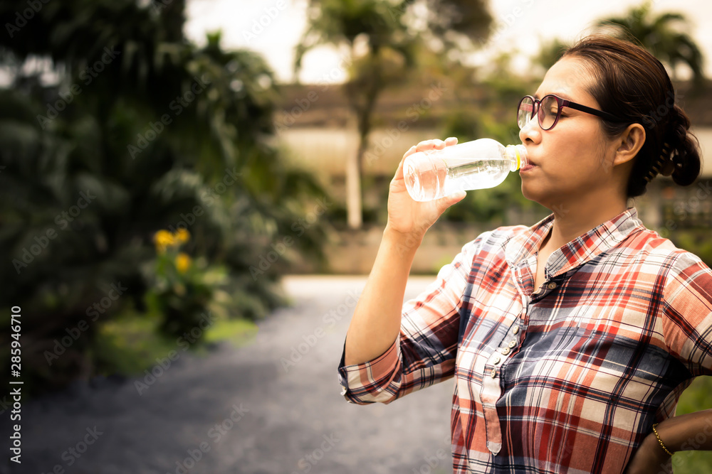 Women wearing glasses drinking water in plastic bottles on the roadside Women wearing glasses drinking water in plastic bottles on the roadside