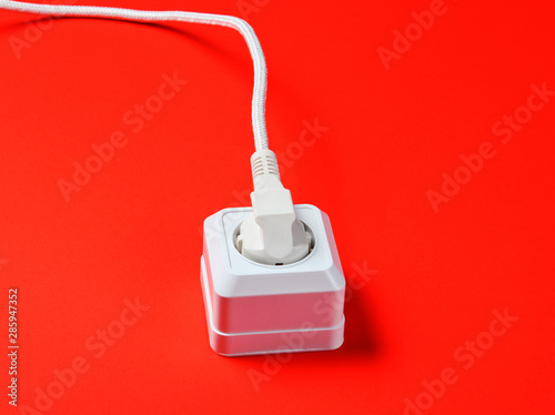 White cable plugged into power outlet on red background