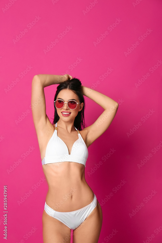 Obraz premium Beautiful young woman in white bikini with sunglasses on pink background
