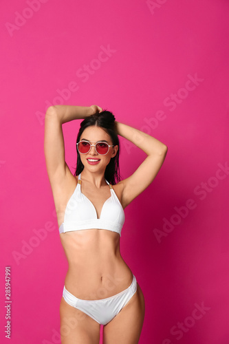 Beautiful young woman in white bikini with sunglasses on pink background © New Africa