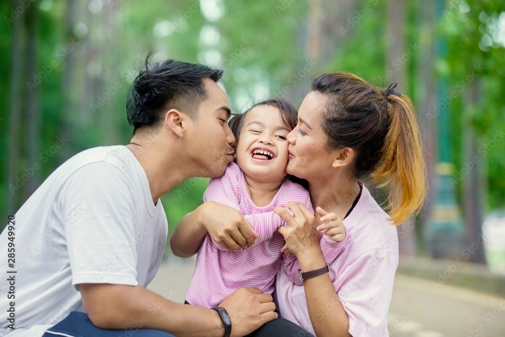 Fototapeta premium Young parents kissing their daughter in the park