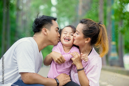 Young parents kissing their daughter in the park © Creativa Images