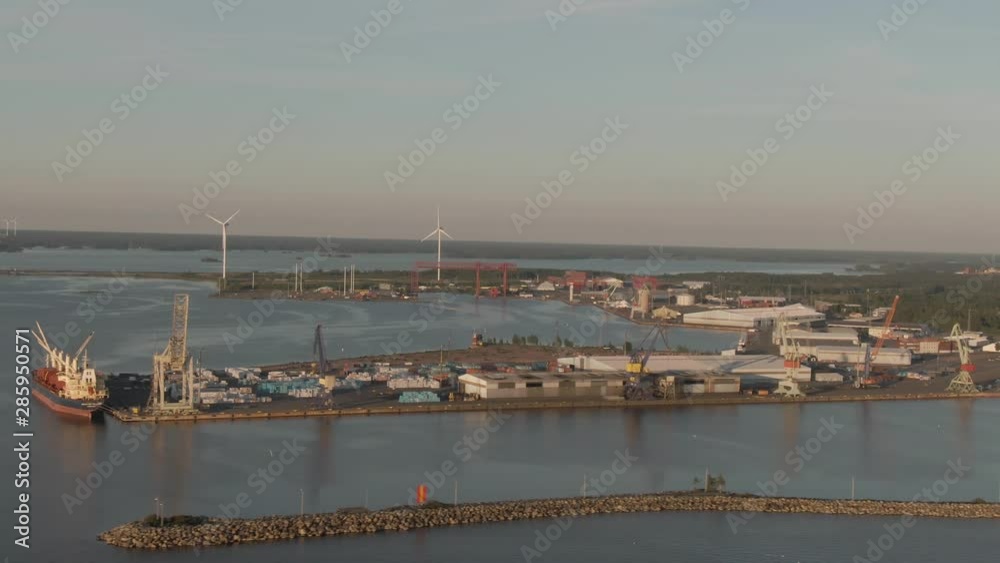 Ship harbor and windmills. Sky and horizon in golden hour. Cranes and rotating mills in background. Drone shot of landscape with port and sea. Ship harbor and windmills. Sky and horizon in golden hour. Cranes and rotating mills in background. Drone shot of landscape with port and sea.