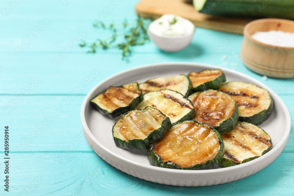 Plate of delicious grilled zucchini slices on light blue wooden table. Space for text