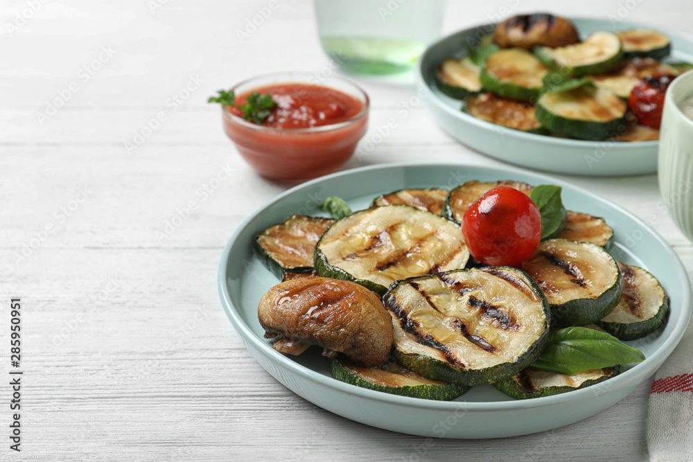 Delicious grilled zucchini slices served on white wooden table. Space for text