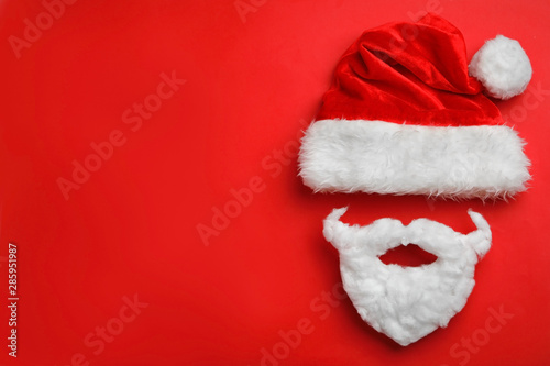 Santa Claus hat with white beard on red background, flat lay. Space for text