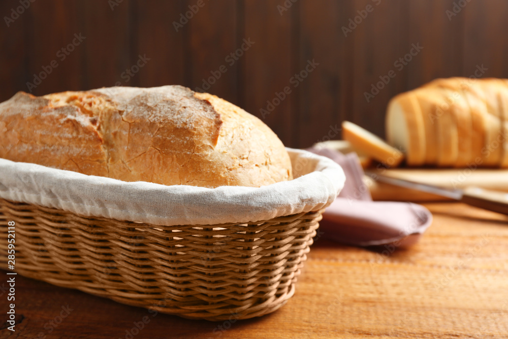 Loaf of tasty fresh bread in wicker basket on wooden table