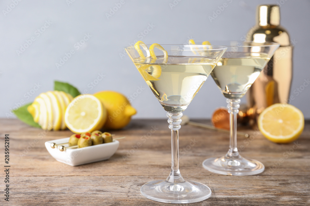 Glasses of lemon drop martini cocktail with zest on wooden table against grey background Glasses of lemon drop martini cocktail with zest on wooden table against grey background