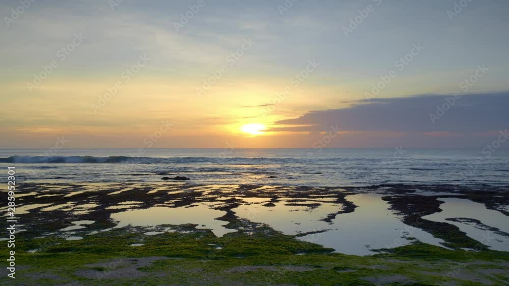 Sunset ocean beach during low tide with high waves on reef with brown and green seaweed Sunset ocean beach during low tide with high waves on reef with brown and green seaweed