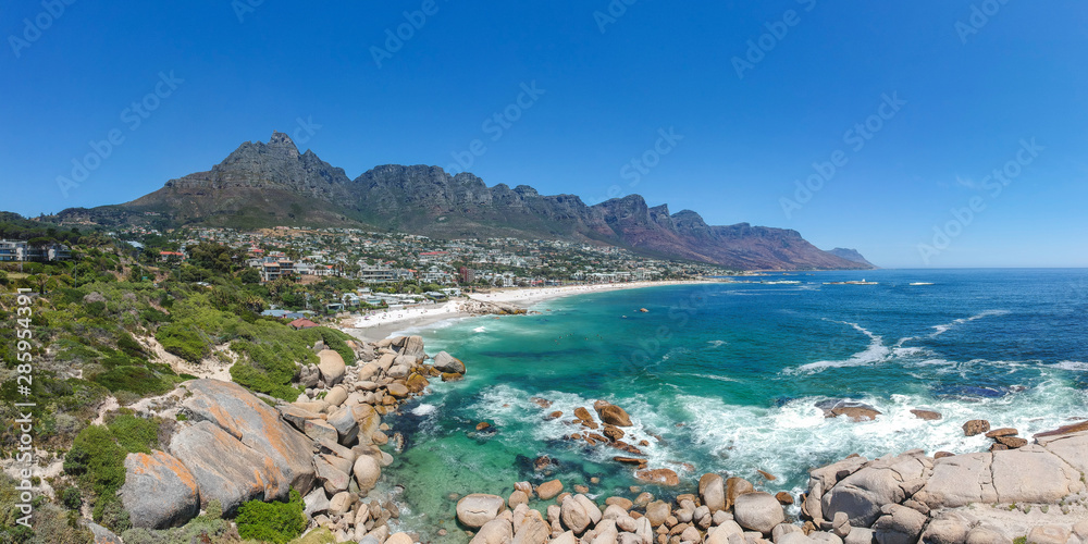 Fototapeta premium Panoramiczny widok z drona w rozmiarze XXL na Camps Bay, zamożne przedmieścia Kapsztadu w RPA. Dzięki białej plaży Camps Bay przyciąga wielu turystów. Dwunastu apostołów w tle pasmo górskie.