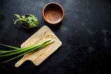 Cooking dinner. Cutting board and herb ingredients. Fresh mint leaves, scallion (green onion), empty natural wooden bowls on stone table, black background, top view, flat lay