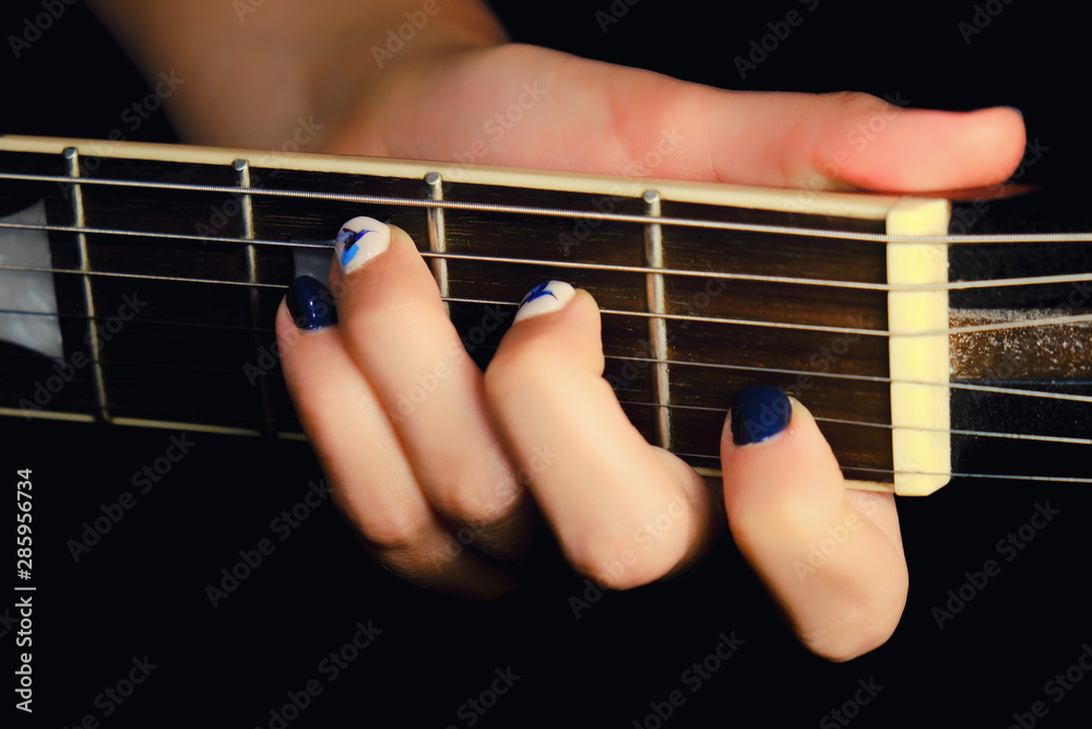 Female hand with manicure lying on the wooden neck of the guitar. Woman guitarist clamped a chord on the strings of the musical instrument.