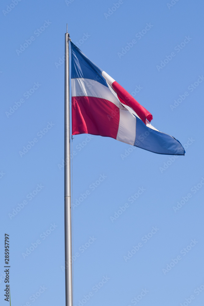 Flag of Dominican Republic (DR) waving in the wind with blue sky on background
